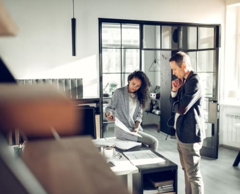 Telling about project. Curly stylish young assistant of interior designer telling him about the project